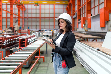 A woman in black suit typing on tablet computer, standing in a factory, inspecting the inventory or...