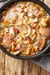 Seared pork tenderloin braised with mushrooms and bacon in a creamy sauce and served with caramelized onions close-up in a frying pan on the table. Vertical top view from above