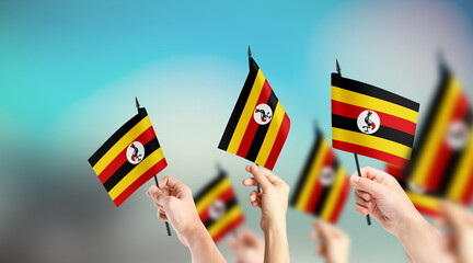 A group of people are holding small flags of Uganda in their hands.