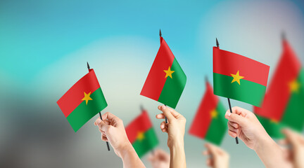 A group of people are holding small flags of Burkina Faso in their hands.