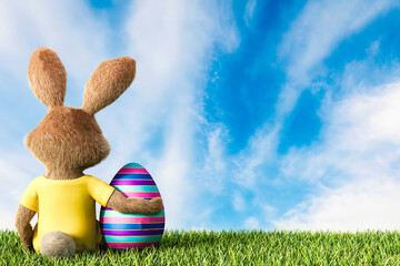 Easter bunny sitting on grass with arm around Easter egg