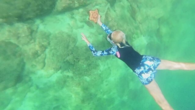 A woman with vibrant yellow fins gracefully holds a starfish while exploring the serene depths near the Chinese wreck dive site in Mirbat town, Dhofar region, Oman.