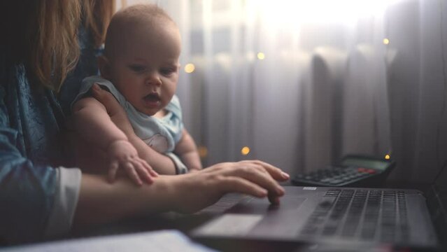 Closeup cropped shot of unrecognizable young busy mother typing working on laptop computer in home office, multitasking and internet search to balance family or working life. Shooting in slow motion.