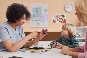 Side view portrait of caring Black woman as doctor showing inhaler to child in pediatricians office at clinic