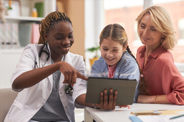 Portrait of smiling female doctor pointing at digital tablet while consulting family in medical clinic for children