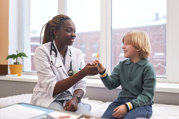 Side view portrait of smiling woman doctor fist bump with little boy in clinic after check up, copy space