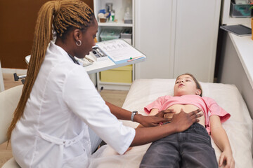 Obraz premium Side view portrait of female doctor palpating stomach of young girl lying on cot in medical clinic