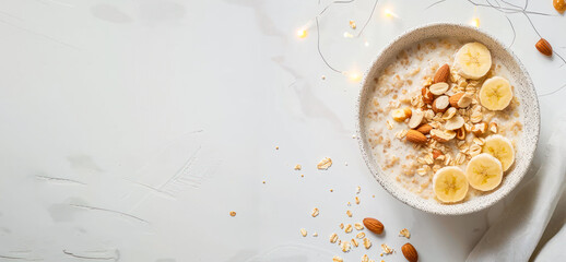 Wheat porridge with peanut butter, nuts and banana in a bowl on light grey background banner. Top...