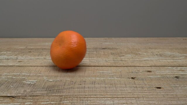 Mandarin rolls and stops in the middle of a wooden surface on a gray background.