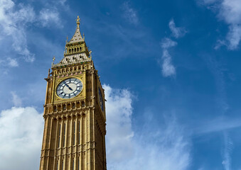 A low angle view of Big Ben against a blue sky with light clouds in Westminster, London, UK. 