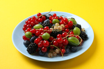 Ripe berries in a plate on a yellow background.