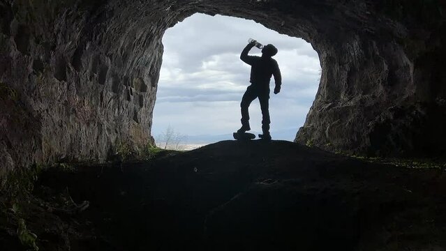 silhouette of man drinking water in cave