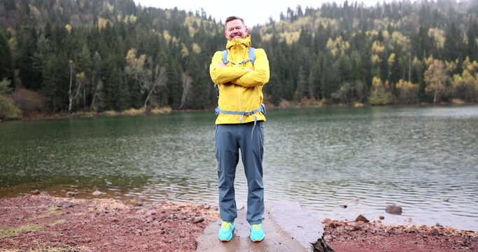 Happy smiling male traveler blogger on background of forest mountains and lake in rain. Traveler tourist and photos for blog and vlog