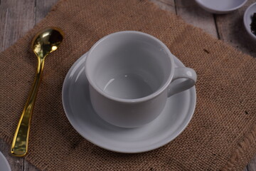 high angle of empty white glass mug or cup with golden spoon on straw matting