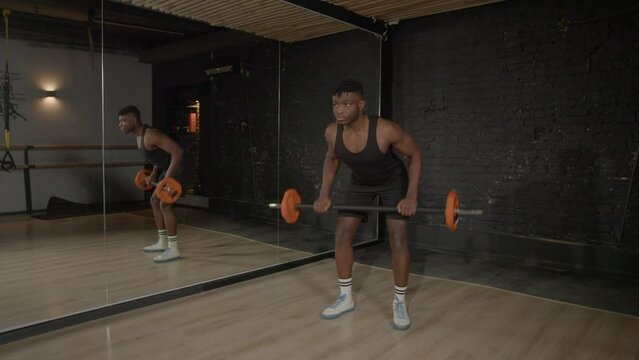 Active motivated sporty muscular build African man doing weightlifting training, practicing barbell row exercise , strengthening upper body and back muscles during indoor workout.