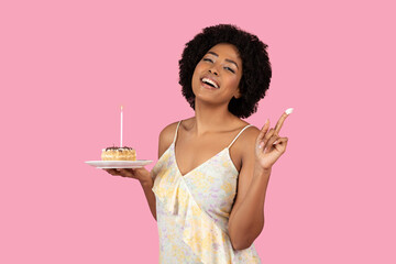 A radiant woman with a joyful smile makes a wish on a lit birthday candle atop a delicious slice of...