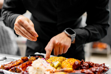 chef cooking tray of assorted grilled food, including ribs, corn, and sausages on kitchen