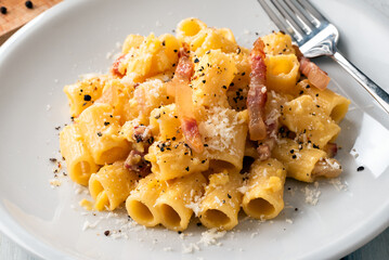 Piatto di deliziosi rigatoni alla carbonara, una ricetta tradizionale di pasta con salsa di uovo, guanciale, pecorino e pepe nero della cucina romana, pasta italiana, cibo europeo  - obrazy, fototapety, plakaty