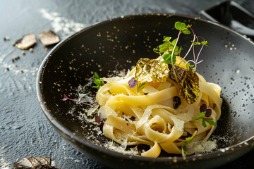 Exquisite truffle pasta garnished with edible gold leaf and microgreens on a dark elegant porcelain dish