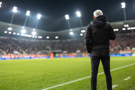 Head coach's back and soccer match at the stadium in the background.