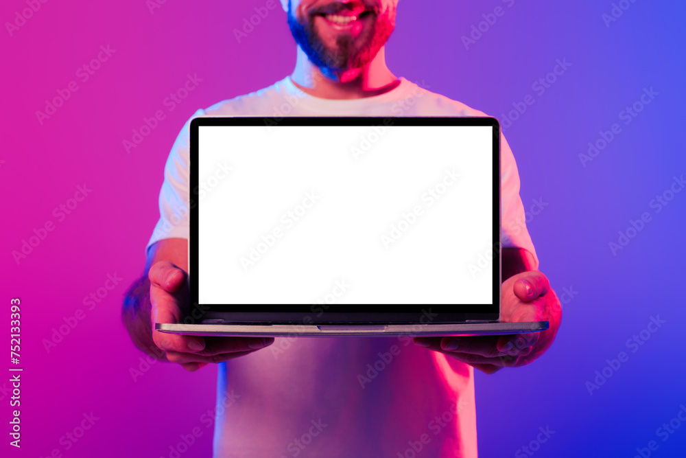 Poster cropped of man showing laptop empty screen in neon studio