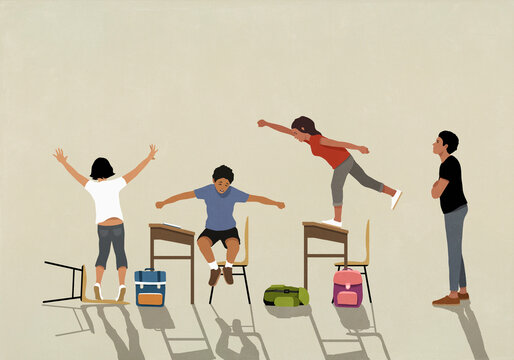 Frustrated teacher watching hyper schoolchildren jumping on desks in classroom
