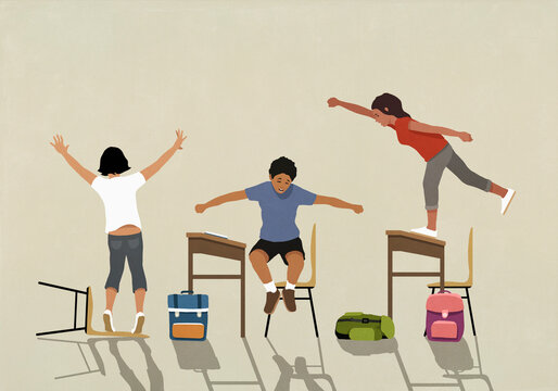 Hyper schoolchildren playing, jumping on desks in classroom
