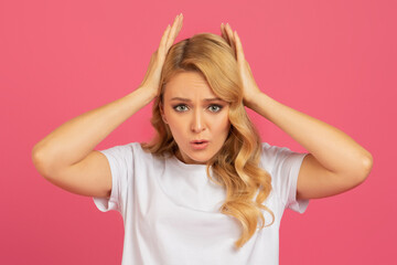 Sad blonde woman touches head expresses discontent against pink background