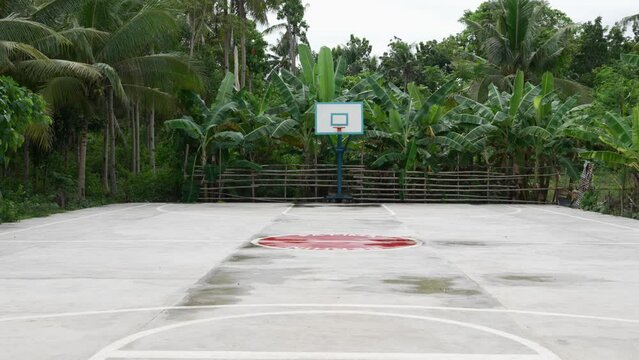 Outdoor basketball court in the Philippines with a blue hoop, surrounded by lush greenery, overcast sky