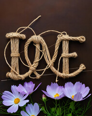 The word love consists of a rope on a brown background. There are blue flowers at the bottom.