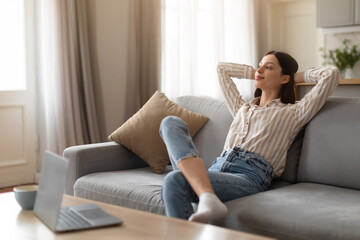 Relaxed young woman lounging on sofa in front of laptop on table