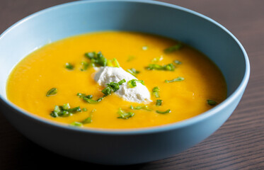 delicious carrot soup in a bowl with cream and green onion close-up