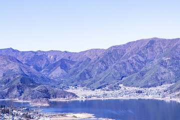 Obraz premium Landscape Forest Lake with mountain blue sky and bright sunlight in background. Hills, lagoon of smoky mountain range covered in white mist and deciduous forest. Dry forests in winter or autumn.