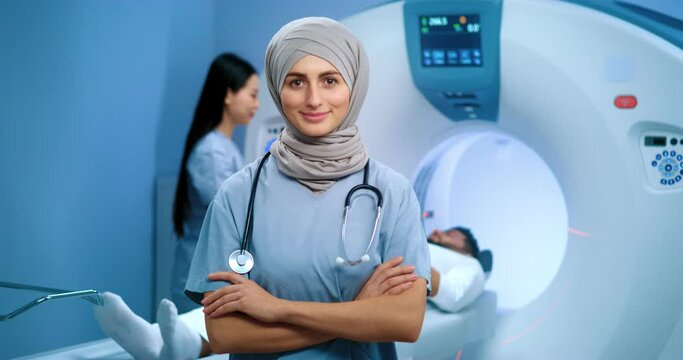 Arabian doctor wearing stethoscope. Doctor in hijab posing with arms crossed. MRI procedure at background. Nurse conducting MRI tomography. Patient lying in MRI capsule. Magnetic resonance tomography.