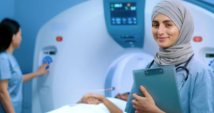 Arabian doctor with stethoscope holding folder. Muslim doctor in hijab. MRI procedure at background. Nurse conducting MRI examination. Patient lying in MRI capsule. Magnetic resonance tomography.