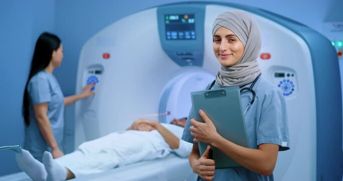 Arabian doctor with stethoscope holding folder. Muslim doctor in hijab. MRI procedure at background. Nurse conducting MRI examination. Patient lying in CT scanner. Magnetic resonance tomography.