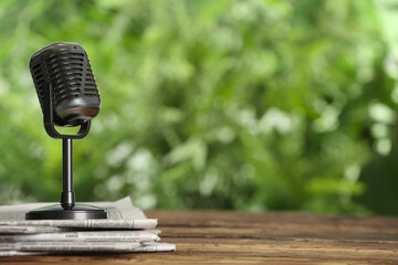 Newspapers and vintage microphone on wooden table against blurred green background, space for text....