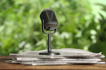 Newspapers and vintage microphone on wooden table against blurred green background. Journalist's work - obrazy, fototapety, plakaty