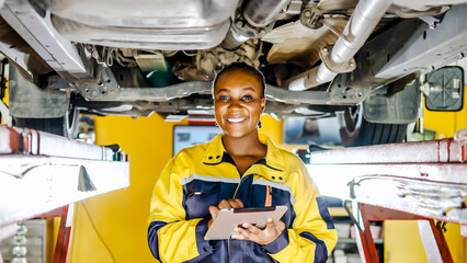 American african Black woman walks under car with using tablet to search for approval and diagnose car breakdowns, use of technologies for repair of vehicle. Auto service and maintenance