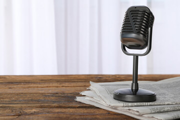 Newspapers and vintage microphone on wooden table, space for text. Journalist's work