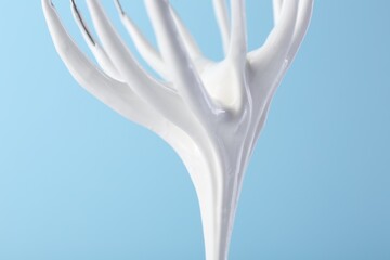 Whisk with whipped cream on light blue background, closeup