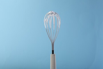 Whisk with whipped cream on light blue background