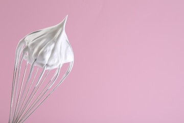 Whisk with whipped cream on pink background. Space for text