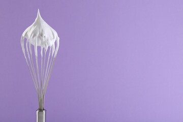 Whisk with whipped cream on violet background. Space for text