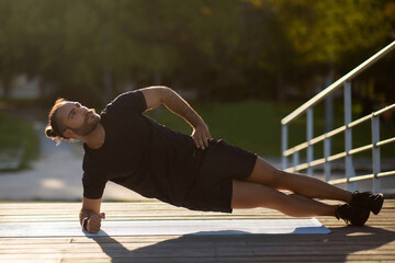 Muscular guy in sportswear doing side elbow plank exercise outside