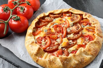 Tasty galette with tomato and cheese (Caprese galette) on dark table, closeup