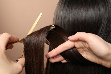 Hairdresser cutting client's hair with scissors on beige background, closeup