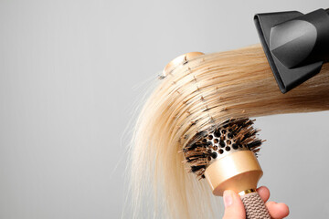 Hairdresser blow drying client's hair on light grey background, closeup. Space for text