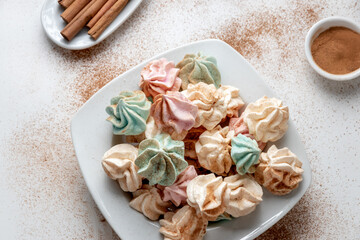 Freshly baked colored French meringue on a white plate on a white background sprinkled with cinnamon