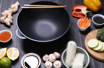 Empty iron wok, chopsticks and ingredients on dark grey wooden table